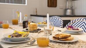 Een ontbijt met pannenkoeken, toast, sap en ontbijtgranen op een tafel.
