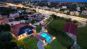 An aerial view of a residential area with houses, a swimming pool, and a road. - 3 Roses Residence in Afandou (Αφάντου)