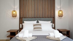 A neatly made bed with white linens and a striped pillow, flanked by wooden nightstands and a headboard with vertical slats. - 3 Roses Residence in Afandou (Αφάντου)