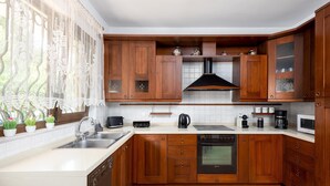 A kitchen with wooden cabinets, a dishwasher, a stove, and a window with plants. - 3 Roses Residence in Afandou (Αφάντου)