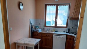 Une cuisine avec une fenêtre, des meubles en bois, un plan de travail blanc et un lave-vaisselle blanc.