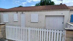 Un bâtiment avec un toit en tuiles, des volets blancs et une clôture en bois peinte en blanc.