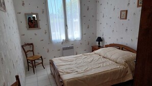 Une chambre à coucher avec un lit, une chaise, une table de chevet, une fenêtre et un papier peint à motifs.