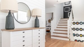 Un interior moderno con un aparador blanco, dos lámparas, un espejo, una escalera con escalones de madera y una pared con discos de vinilo.