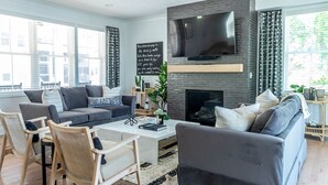 Una sala de estar moderna con chimenea, asientos cómodos y un televisor grande montado en la pared.