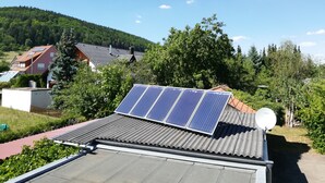 Zona residencial con paneles solares en un tejado, rodeada de vegetación y casas.
