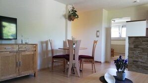 Un comedor con mesa y sillas de madera, televisor en la pared y una pared de acento de piedra.