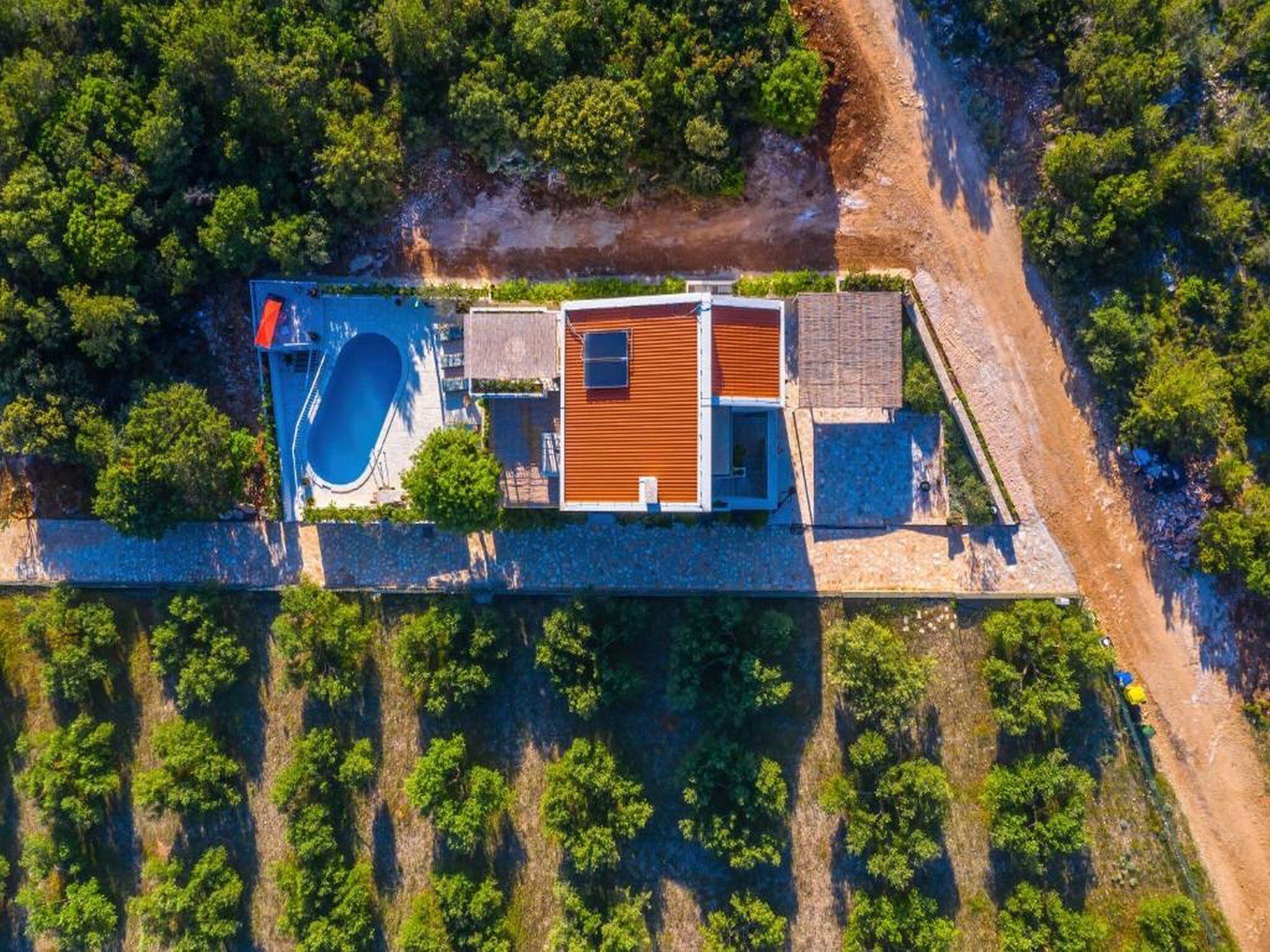 Luchtbeeld van een modern huis met een zwembad, een houten terras en een pad van stenen.
