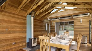 Un interior de madera con comedor, estufa empotrada y cocina visible a través de una puerta abierta.