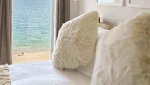 Un dormitorio con vista al mar, una cama con almohadillas blancas y mullidas, y una lámpara fijada a la pared.