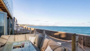Un patio frente al mar con una mesa de vidrio, asientos acolchados y vista al océano.