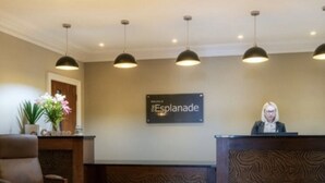 Un área de recepción con un letrero que dice "Esplanade", un mostrador de recepción, una silla e iluminación colgante.