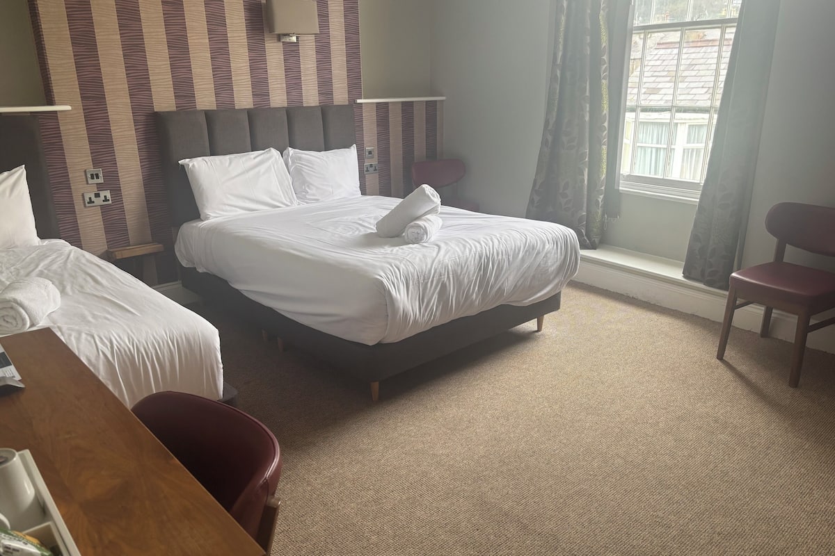A hotel room with two beds, a desk, a chair, and a window with curtains.