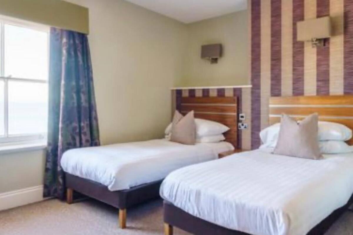 A hotel room with two single beds, a window with curtains, and a striped wall design.
