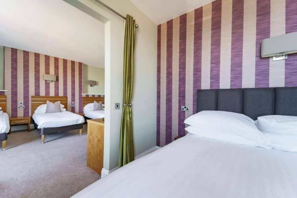 A hotel room with two beds, a green curtain, and striped wallpaper.