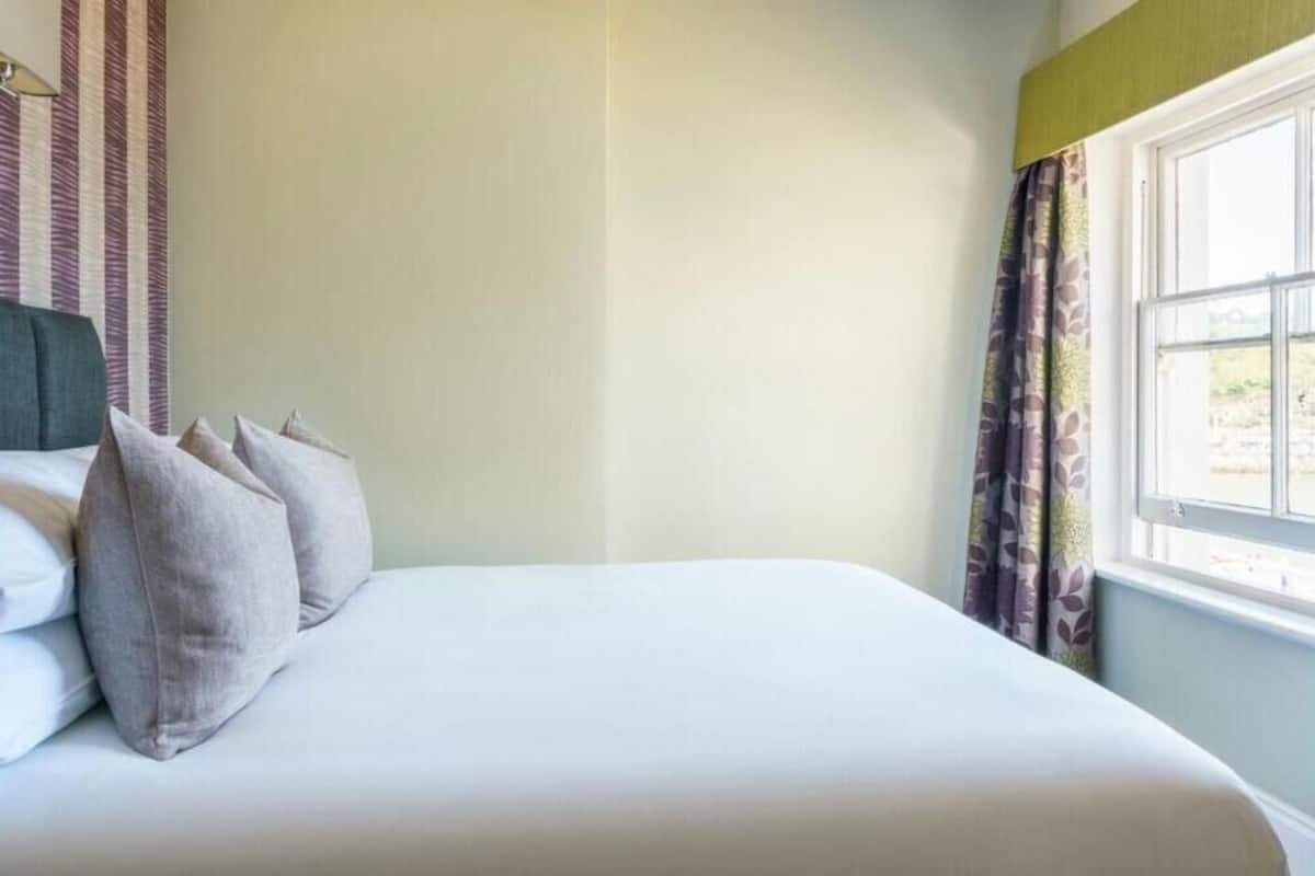 A hotel room with a neatly made bed, a window with curtains, and a striped wall pattern.
