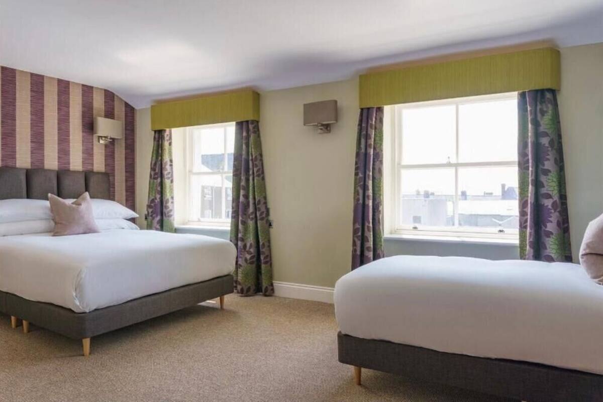 A hotel room with two beds, a striped wall, a window with curtains, and a city view.