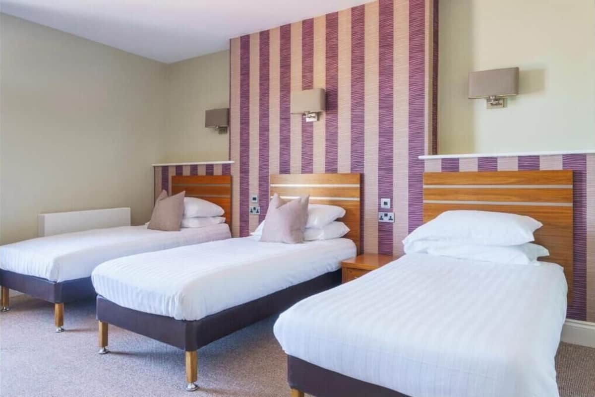 A hotel room with three single beds, each with a wooden headboard and white bedding.