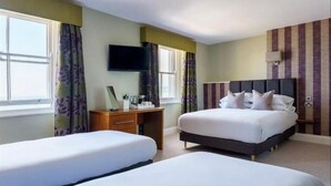 Habitación de hotel con dos camas individuales, un escritorio con silla, un televisor de pantalla plana montado en la pared y una ventana con cortinas.