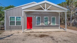 A single-story building with a red door, two windows, and a covered porch. - RR 464 Sattler Haus (New Braunfels)