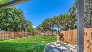 A backyard with a paved pathway, a wooden fence, and trees. - RR 464 Sattler Haus (New Braunfels)