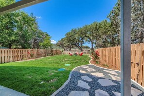 A backyard with a paved pathway, a wooden fence, and trees.