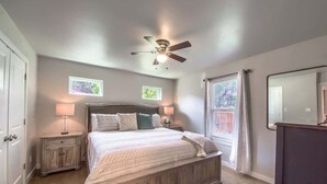 A bedroom with a bed, nightstands, a ceiling fan, a window with curtains, and a mirror. - RR 464 Sattler Haus (New Braunfels)