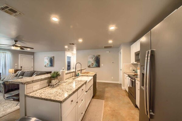 A modern kitchen with granite countertops, stainless steel appliances, and recessed ceiling lighting.