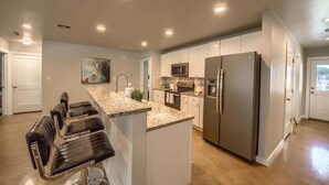 A modern kitchen with a central island, stainless steel appliances, and a bar seating area. - RR 464 Sattler Haus (New Braunfels)