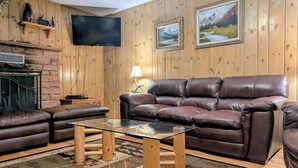 A cozy living room with a leather sofa, a glass coffee table, a fireplace, wooden walls, and framed pictures. - CASCADE RETREAT IN MOUNTAIN SETTING, NEAR PIKES PEAK, MINUTES TO MANITOU SPRINGS (Manitou Springs)