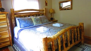 A wooden bed with a headboard, a bedside table with a lamp, and a wall-mounted mirror. - CASCADE RETREAT IN MOUNTAIN SETTING, NEAR PIKES PEAK, MINUTES TO MANITOU SPRINGS (Manitou Springs)