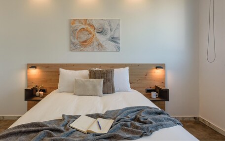 A neatly made bed with a blue blanket, a book, and a cup on a bedside table.