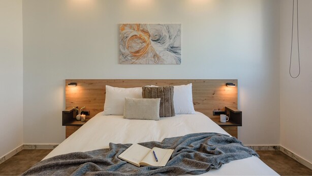 A neatly made bed with a blue blanket, a book, and a cup on a bedside table. - Zed Smart Property by Airstay (Spata-Artemida)