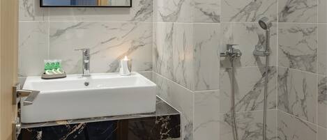 Un baño con lavamanos de mármol, un espejo, ducha y toallero.