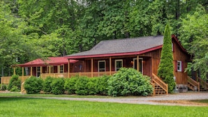 A wooden cabin with a porch, surrounded by lush greenery and trees. - Twin Creeks Cabin - RIVER FRONT! *Hot tub* 4 acres! Pets OK (Deep Gap)