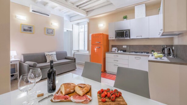 Una cocina moderna con armarios blancos, un refrigerador naranja y un comedor con una mesa blanca dispuesta para dos.