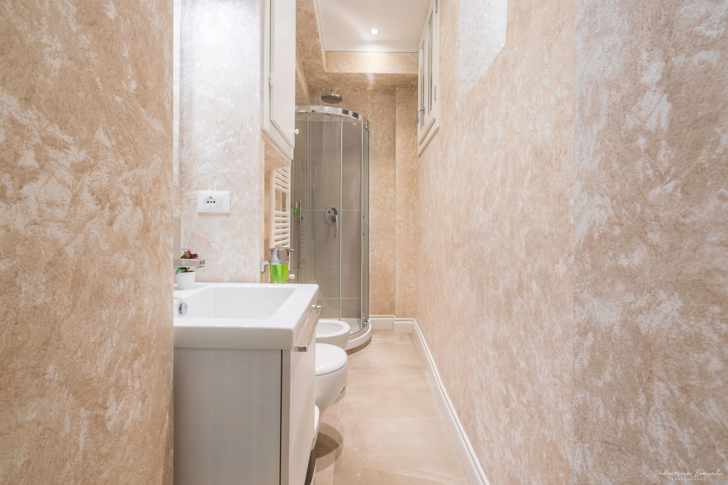 Un baño estrecho con ducha, inodoro y lavamanos.