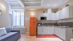 Una cocina moderna con armarios blancos, un refrigerador naranja y un sofá gris.