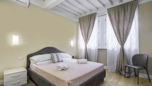 Un dormitorio con cama, mesita de noche, silla y cortinas.