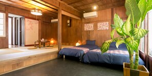 Una habitación de estilo japonés tradicional con suelo de tatami, dos camas con ropa de cama azul, techo de madera y una planta verde grande.