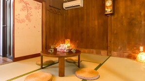 A traditional Japanese room with tatami flooring, a low table with a floral table runner, and a wall-mounted clock.