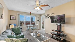 A living room with a ceiling fan, a TV, a glass coffee table, a sofa, and a dining area with chairs and a table.