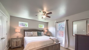 Un dormitorio con cama, mesitas de noche, ventilador de techo, ventana con vistas y un espejo.