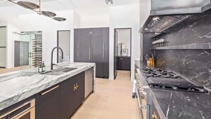 A modern kitchen with a marble countertop, black cabinets, and a stainless steel range hood. - Designer Retreat | Heated Pool & Chefs Kitchen (Scottsdale)
