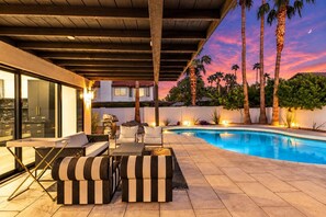 A poolside area with a modern outdoor seating arrangement, a pool, and a view of palm trees against a sunset sky. - THe Ashcroft | FREE Heated Pool | Designer Retreat (Scottsdale)