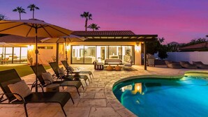 A poolside area with lounge chairs and umbrellas, a pool, and a building with large windows and a patio. - Designer Retreat | Heated Pool & Chefs Kitchen (Scottsdale)