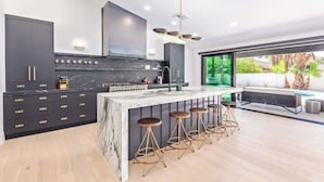 A modern kitchen with dark cabinetry, a marble island, and bar stools. - Designer Retreat | Heated Pool & Chefs Kitchen (Scottsdale)
