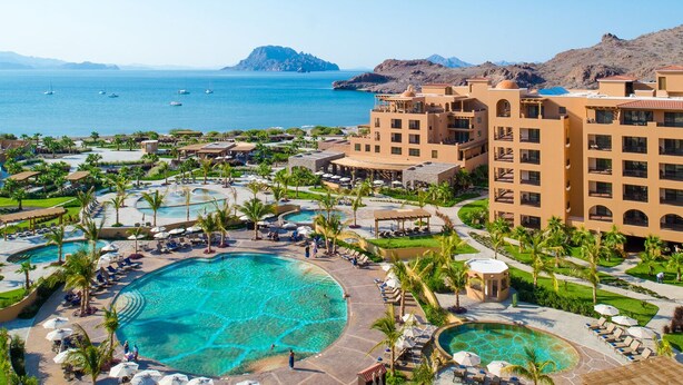 Un resort con diverse piscine, palme e vista sul mare.