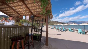 Un bar sulla spiaggia con tetto di paglia, posti a sedere all'aperto e vista sulla spiaggia e sulle montagne.
