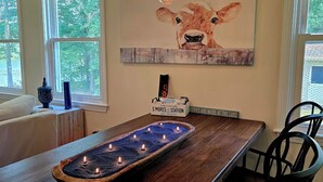 Un coin repas avec une table en bois, des chaises noires, un chandelier servant de centre de table et un tableau représentant une vache accroché au mur.
